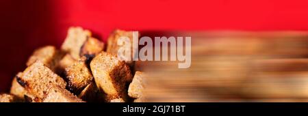 Croûtons de pain noir sur fond rouge. Délicieux craquelins croquants frits. Faible profondeur de champ. Bannière panoramique sur la nourriture Banque D'Images
