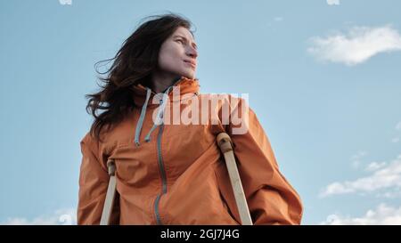 Une femme sur des béquilles marche le long de la rive du lac. Plage de sable sur fond de lac calme et de nuages à l'horizon Banque D'Images