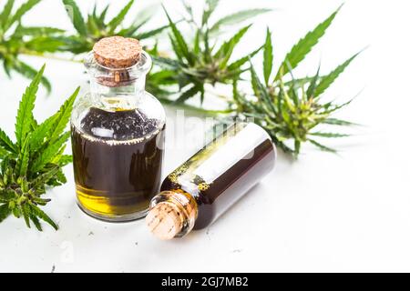 Huile de CBD en bouteilles de verre et feuilles de cannabis à la table blanche. Banque D'Images