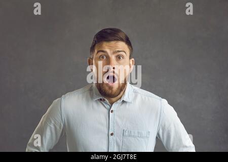 Portrait d'un jeune homme avec une expression surprise criant WOW sur un fond gris. Banque D'Images