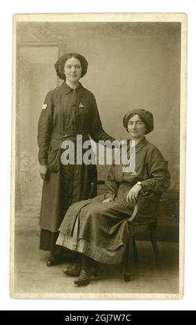 Portrait original en studio de la première Guerre mondiale d'une paire de femmes ouvrières attirantes portant des badges du ministère des munitions « en service de guerre », Londres ou Woking (Surrey), Angleterre, Royaume-Uni vers 1917 Banque D'Images