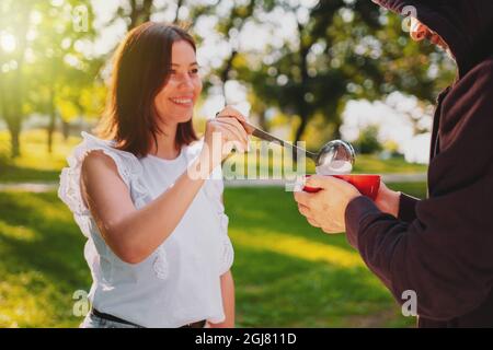 Une jeune femme heureuse verse de la soupe dans le bol rouge à l'aide d'une louche et un homme sans abri maintient le bol dans ses mains. Banque D'Images