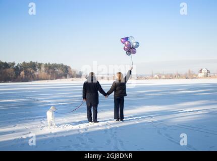 amoureux méconnaissables homme et femme tenant les mains marcher le chien dans la neige en hiver. sentiments tendres, humeur festive. Saint-Valentin ensemble Banque D'Images