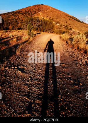 Longue ombre nocturne d'un seul homme en randonnée dans la montagne sur la route de terre Banque D'Images