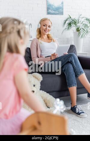 bonne femme regardant la fille floue tout en étant assise sur un canapé dans un casque Banque D'Images