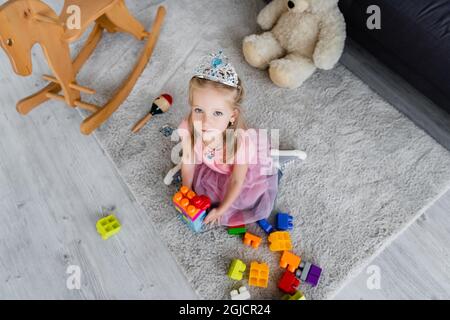 vue en hauteur d'un enfant dans une couronne de jouets jouant avec des blocs de construction colorés près des jouets au sol Banque D'Images