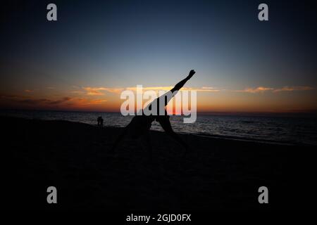 Silhouette d'un homme qui fait de l'exercice sur une roue à cardans sur la plage au coucher du soleil avec la mer et le ciel en arrière-plan Banque D'Images