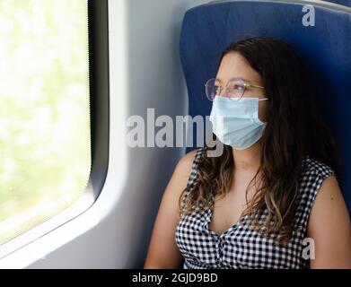 Femme d'affaires avec masque de protection et lunettes de vue hors de la fenêtre du train dans la pensée. Jeune femme pensant en voyageant en train Banque D'Images