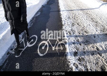 Une personne qui marche sur une piste cyclable, une piste cyclable, qui s'est dégagée de la neige à côté d'une chaussée enneigée et glacée. Photo: Pontus Lundahl / TT / code 10050 Banque D'Images