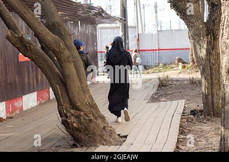 Une femme dans une burqa noire descend la rue. Une femme musulmane marche à travers la ville. Un citadin de l'arrière. Banque D'Images