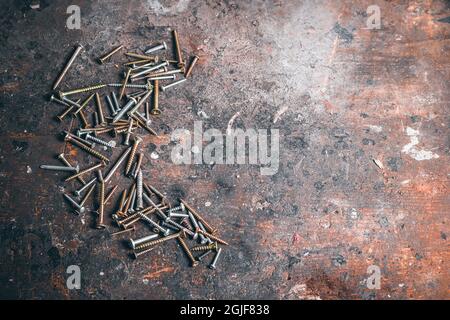 Beaucoup de vis sur établi en bois. Différents types de vis sur une table dans un atelier. Jeu de vis. Abstraction de construction. Arrière-plan industriel. Banque D'Images