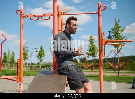 Portrait confiant de macho beau, homme sportif attrayant, européen caucasien de construction musculaire athlète en vêtements de sport sur le fond des barres transversales Banque D'Images