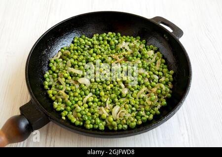 Petits pois verts sautés maison dans une poêle en fonte sur fond de bois blanc, vue latérale. Banque D'Images