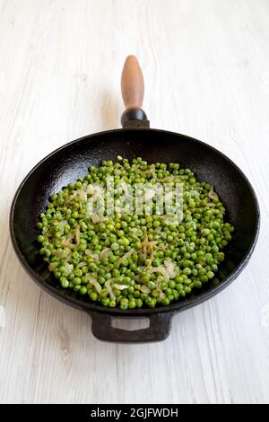 Petits pois verts sautés maison dans une poêle en fonte sur fond de bois blanc, vue latérale. Banque D'Images