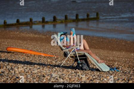 Femme lisant sur la plage dans une chaise paresseuse en été. Banque D'Images