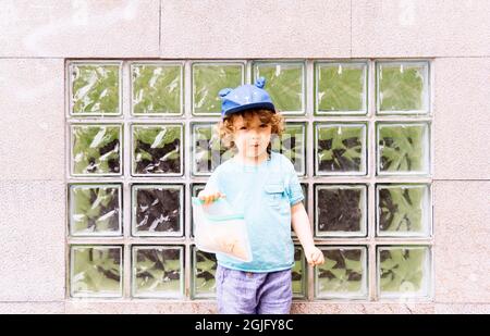 garçon de trois ans avec un chapeau bleu ayant une collation dans la rue Banque D'Images