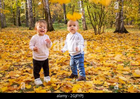 Les enfants gais attrapent des feuilles d'érable tombant dans le parc de la ville d'automne. Banque D'Images