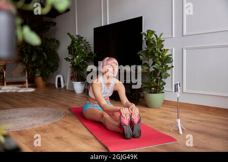 Happy Fitness Trainer enregistre une nouvelle vidéo pour le blog faisant un virage vers l'avant tout en étant assis sur le tapis Banque D'Images