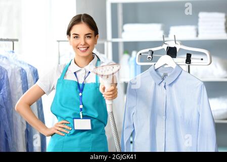 Femme travaillant avec un défroisseur dans un sèche-linge moderne Banque D'Images