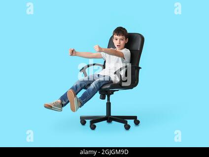 Petit garçon avec volant imaginaire assis dans la chaise sur fond de couleur Banque D'Images