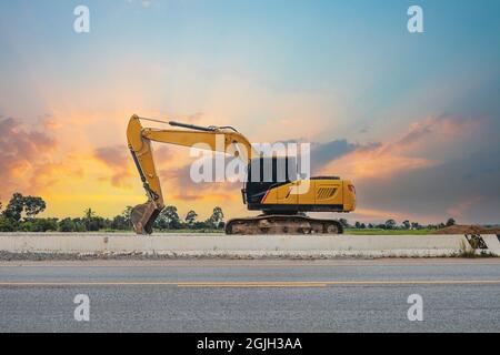 Une pelle rétro jaune garée sur le bord de la route dans le ciel au coucher du soleil. Banque D'Images