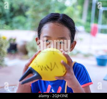 mignonne petite fille asiatique soufflant des ballons jaunes Banque D'Images