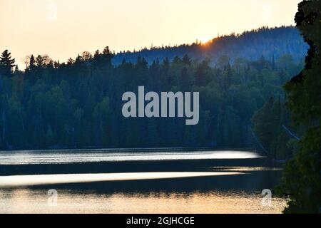 Le soleil se couche derrière les collines boisées lors d'une chaude journée d'été sur le lac Bass, près de Thunder Bay, Ontario, Canada. Banque D'Images