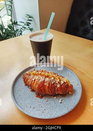 Croissant sucré avec caramel et banane et cappuccino sur la table. Petit déjeuner dans un café. Banque D'Images