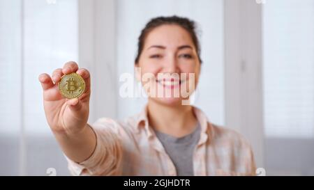 Jeune brune floue tenant le bitcoin doré dans sa main Banque D'Images