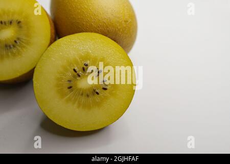 Un Kiwifruit doré ou une groseille chinoise (Actinidia chinensis) coupé en diagonale et une baie entière sur fond blanc Banque D'Images