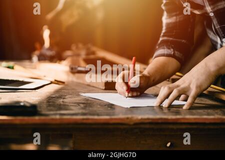 gros plan main de travail mâle à l'aide d'un crayon pour dessiner une pièce en bois de conception de dépouille dans un atelier de bricolage. Banque D'Images