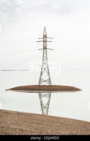 Tour de puissance de transmission à haute tension ou pylône d'électricité installé sur une île artificielle faite par l'homme dans la mer Morte en Israël, par une journée nuageux Banque D'Images