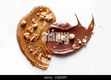 Vue de dessus de savoureux beurre d'arachide et de pâte de chocolat arrosé de noix écrasées placées sur une table blanche Banque D'Images