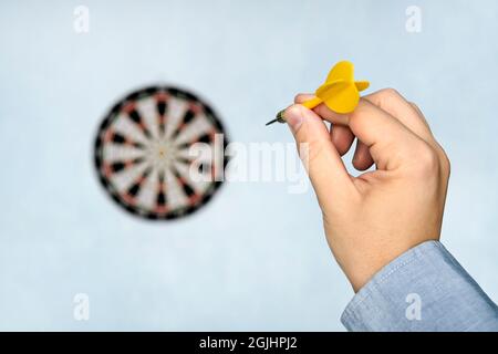 Une main tenant un dart se prépare à viser le dartboard sur le mur bleu. La main d'un homme lance un dart à la cible. Banque D'Images