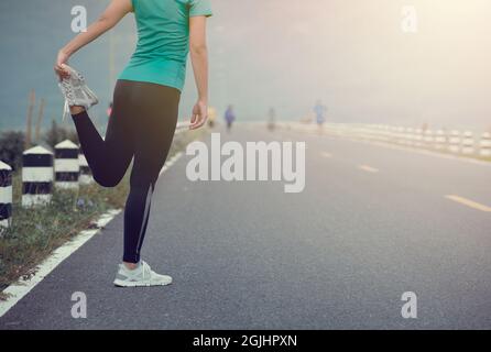 Jeune femme coureur qui s'étire les jambes avant de courir sur la route. Banque D'Images