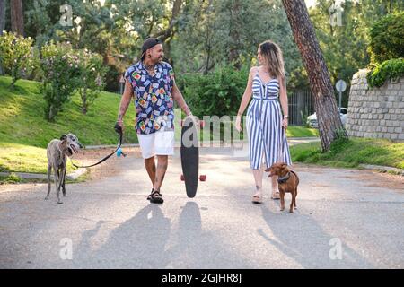 Jeune couple tatoué marchant leurs chiens et portant une longue planche. Banque D'Images