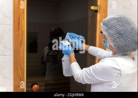 Une femme en gants et costume de protection effectuant le nettoyage et la désinfection dans les espaces publics de sauna.Desinfection avec un spray antibactérien à l'hôpital . Banque D'Images