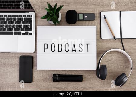 concept de podcast : fond plat, gros plan de la visionneuse avec mot de podcast sur la table avec ordinateur portable, microphone, casque, smartphone et bloc-notes Banque D'Images