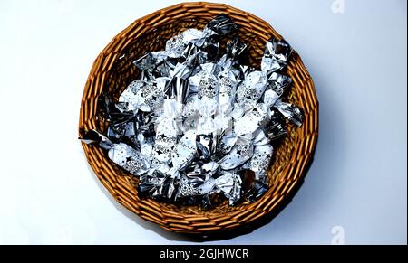 Bonbons au chocolat blanc et argent emballés dans un panier en osier brun sur fond blanc Banque D'Images