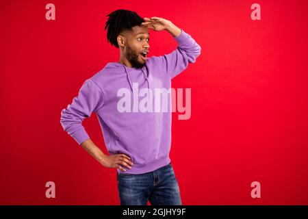 Portrait d'un sympathique brunet gai stupéfié gars regardant loin de l'espace de copie isolé sur fond rouge vif de couleur Banque D'Images