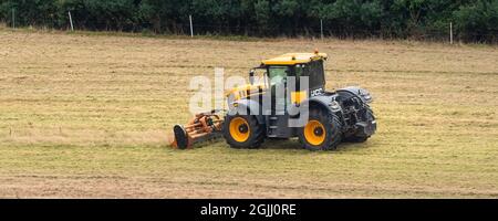 Une image panoramique d'un tracteur agricole à grande vitesse JCB Fastrac 4220 avec un coupe-branches à fléaux Teagle travaillant dans un champ à Newquay en Cornouailles. Banque D'Images