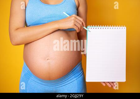 Une femme enceinte sur fond coloré tient un bloc-notes ouvert et un stylo. Copier-coller maquette. Photo de haute qualité Banque D'Images