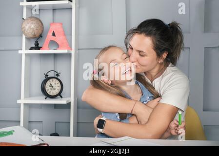 Fille d'école positive avec la mère apprenant à la maison, embrassant et rire. Éducation familiale Banque D'Images