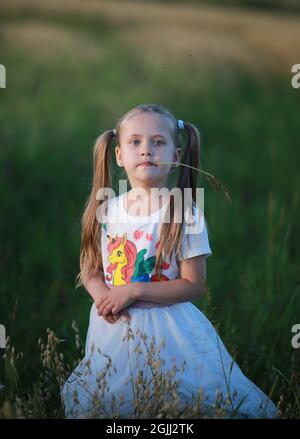Une fille à deux queues, tenant une lame d'herbe dans sa bouche vêtue d'un t-short avec une licorne, marche dans un champ. Banque D'Images