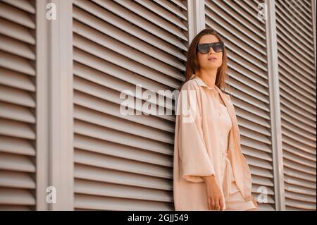 Une jolie fille en beige et en lunettes de soleil posant Banque D'Images