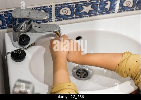 un petit enfant lave ses mains avec de l'eau courante sous le robinet dans un petit lavabo à la maison dans la salle de bains. les enfants sont propres et concept d'hygiène personnelle Banque D'Images