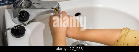 un petit enfant lave ses mains avec de l'eau courante sous le robinet dans un petit lavabo à la maison dans la salle de bains. les enfants sont propres et concept d'hygiène personnelle Banque D'Images