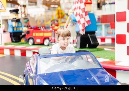 un petit garçon de quatre ans, heureux, s'amuser à faire du sport sur une petite voiture électrique dans un terrain de jeux. les enfants s'amusent dans le jouet a. Banque D'Images