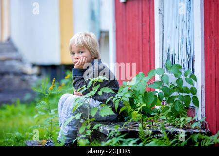 Triste petit enfant, petit garçon d'âge préscolaire, assis sur les escaliers devant la vieille maison ruinée, tristesse Banque D'Images