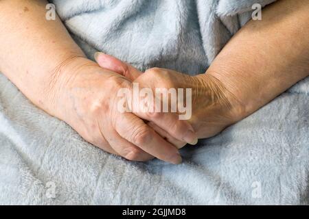 Les mains d'une vieille femme se replient l'une sur l'autre. Femme âgée avec les mains pliées et une couverture bleu clair Banque D'Images